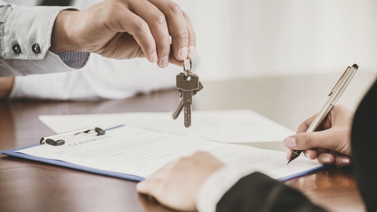 Person dangling a key over someone else who is signing a document